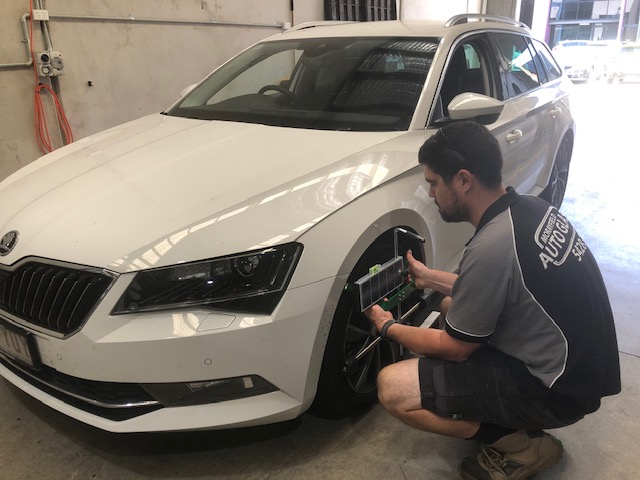 An ADAS-trained technician fitting the wheel-clamp bracket during a calibration in the Buderim workshop