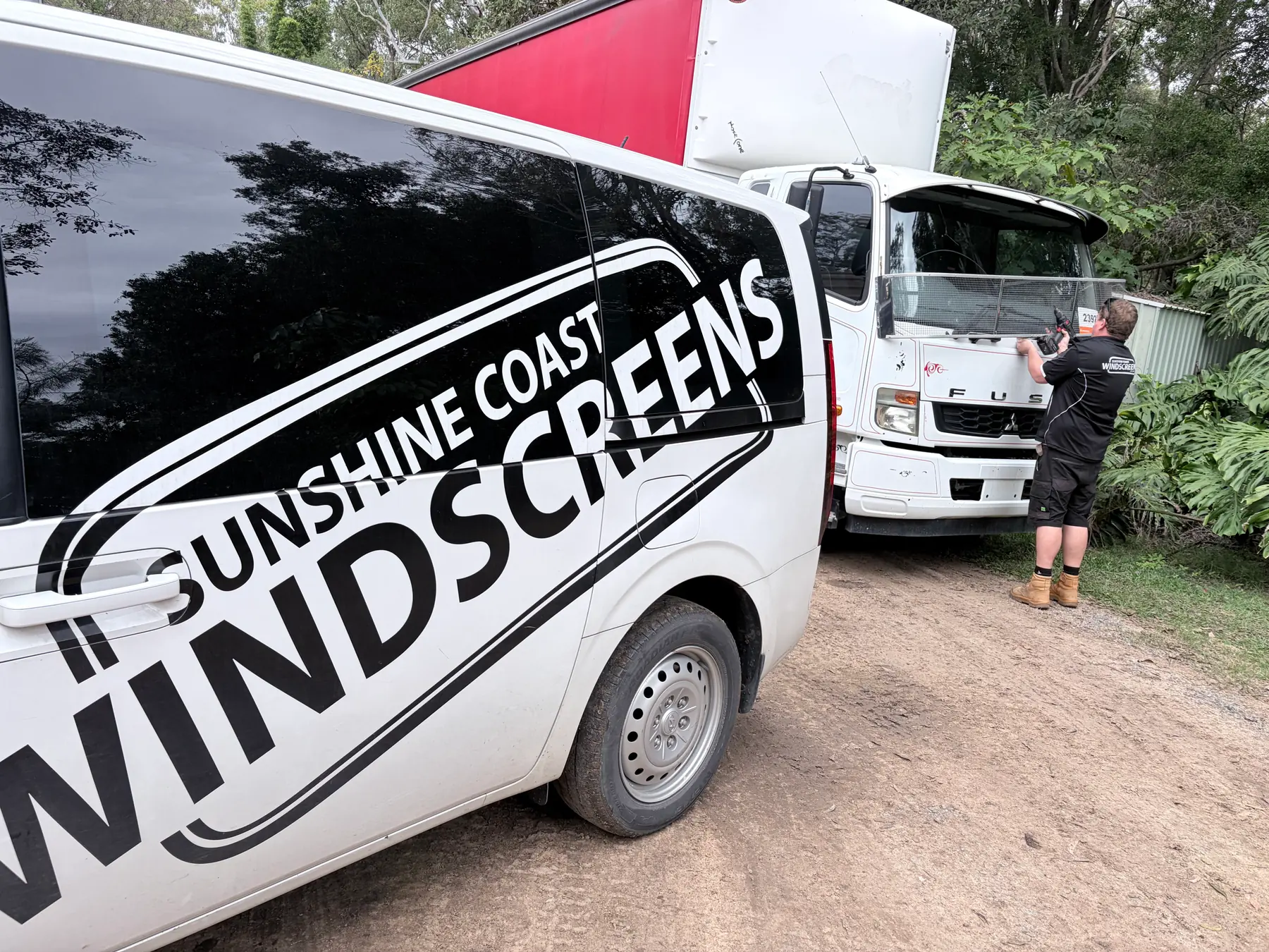 A Sunshine Coast Windscreens technician replacing a truck windscreen beside the branded mobile van