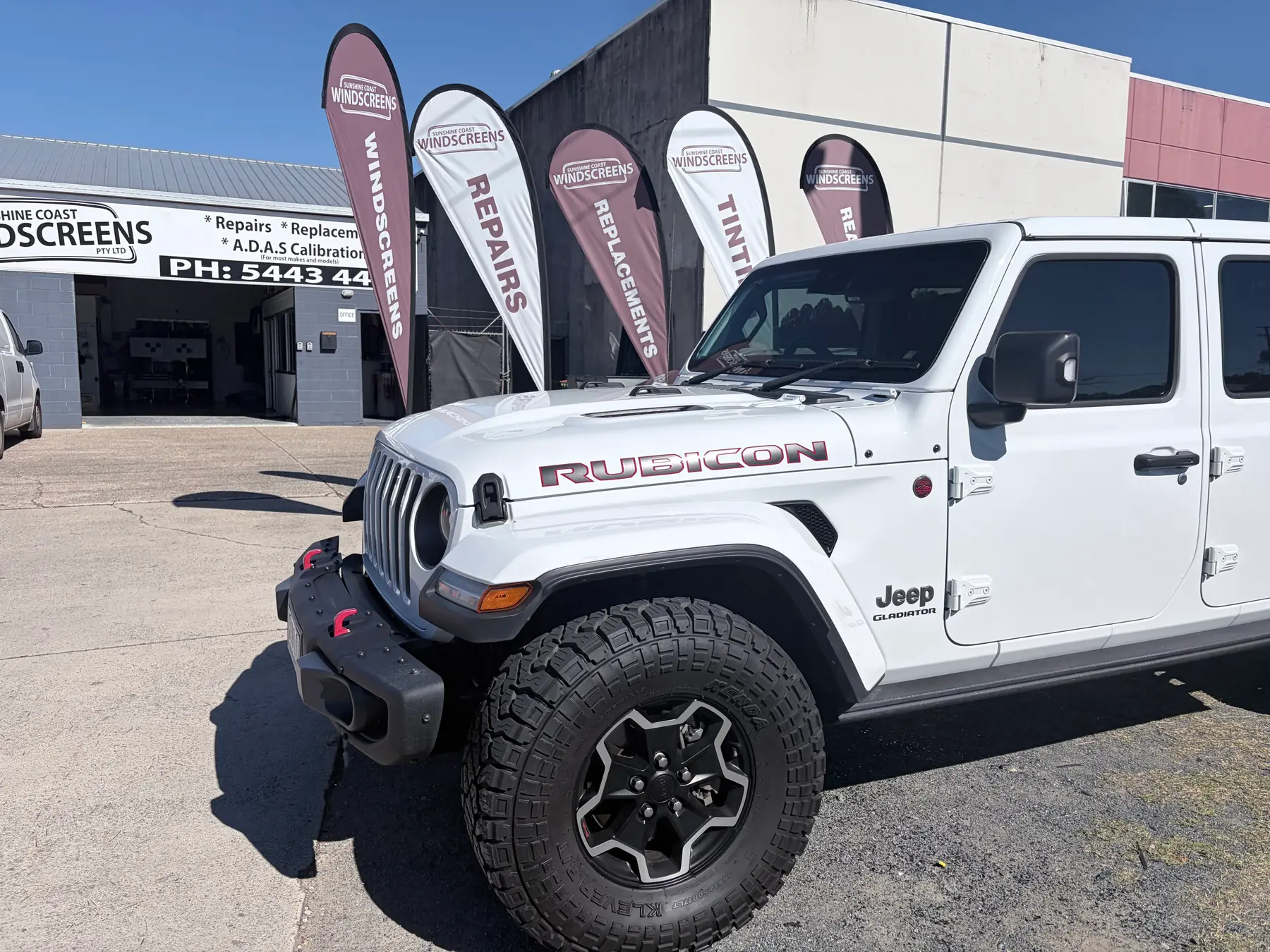 A Jeep and other vehicles outside the Sunshine Coast Windscreens shopfront — every make and model