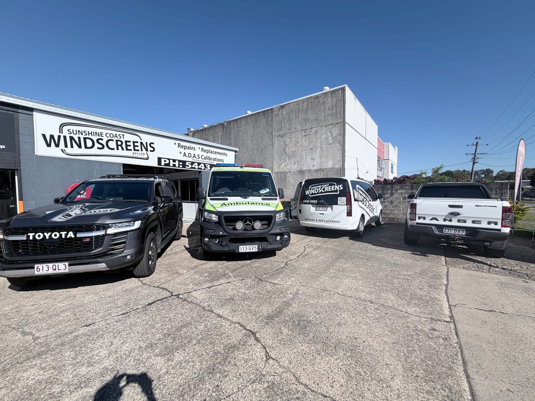 The Sunshine Coast Windscreens shopfront in Buderim with a Toyota LandCruiser, a Queensland ambulance and the branded mobile van in for glass work